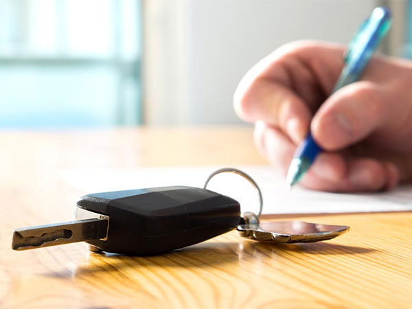 car keys on a table with a person signing rental papers in the background
