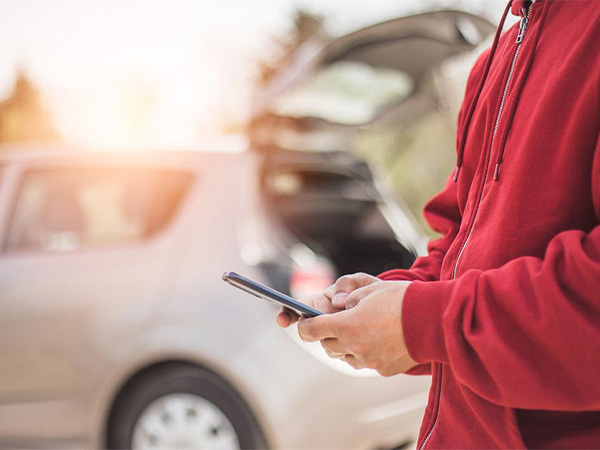 a person on their phone standing besides a car on the road